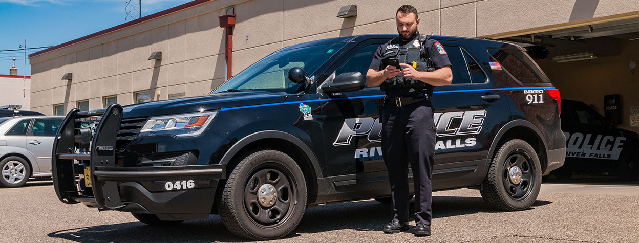 Officer using Aladtec on a mobile device by a squad car